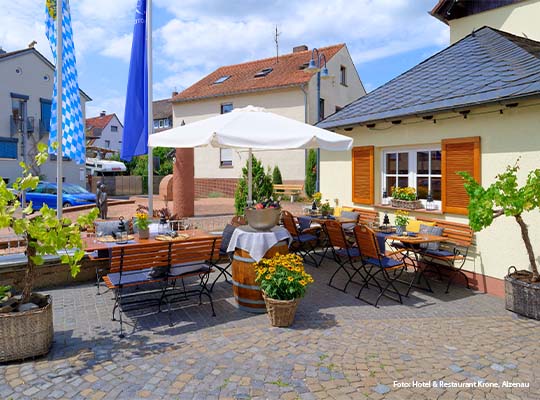 Außenterrasse vom Hotel Krone in Alzenau, mit typischen Biergarten Stühlen und Tischen, es ist außerdem ein Sonnenschirm zu sehen