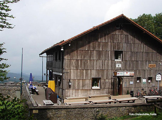 Außenansicht der Enzianhütte, mit Hölzerner Fassade, Bänken vor der Hütte und vier sichtbaren fenstern