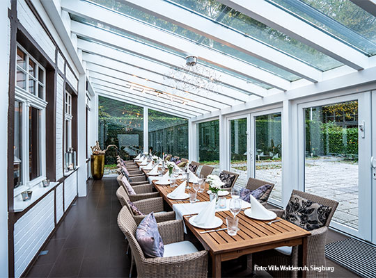 Innenansicht der Indoor-Terrasse, mit einem Langen Tisch an welchem Stühle stehen