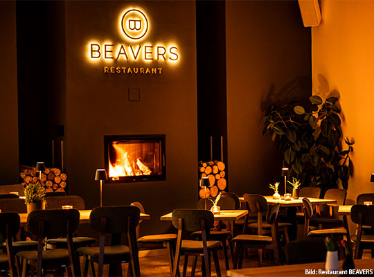 Tische vor Feuerstelle, in einer Wand, über Feuerstelle ist das "BEAVERS" Logo.